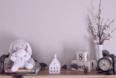 shelf with books, stuffed animals, ceramic house, vase with flowers, calendar, and clock