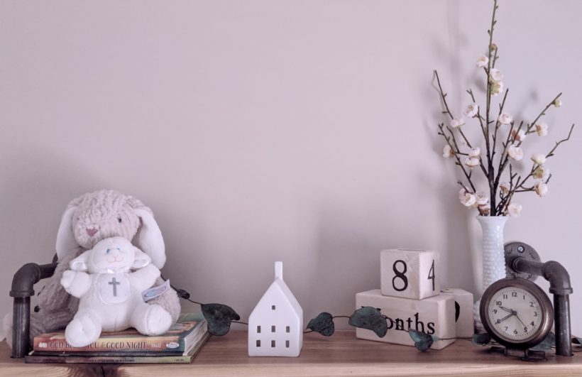 shelf with books, stuffed animals, ceramic house, vase with flowers, calendar, and clock